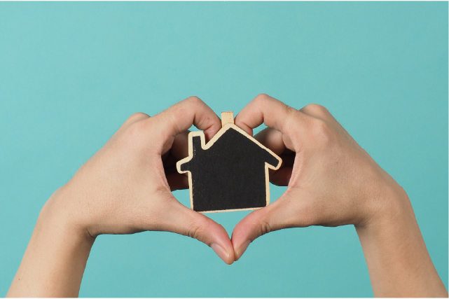 Hands forming a heart shape around a small house model, symbolizing love, ease, and confidence in the home buying process.