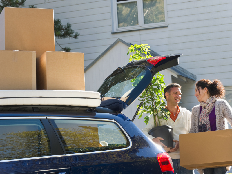  A happy couple unloads moving boxes and a plant from their car, symbolizing a fresh start in a new home.